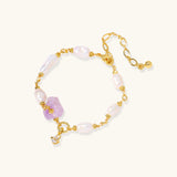 Pulsera bañada en oro con perlas barrocas lustrosas y amatista en bruto color lavanda como pieza central, sobre fondo blanco.