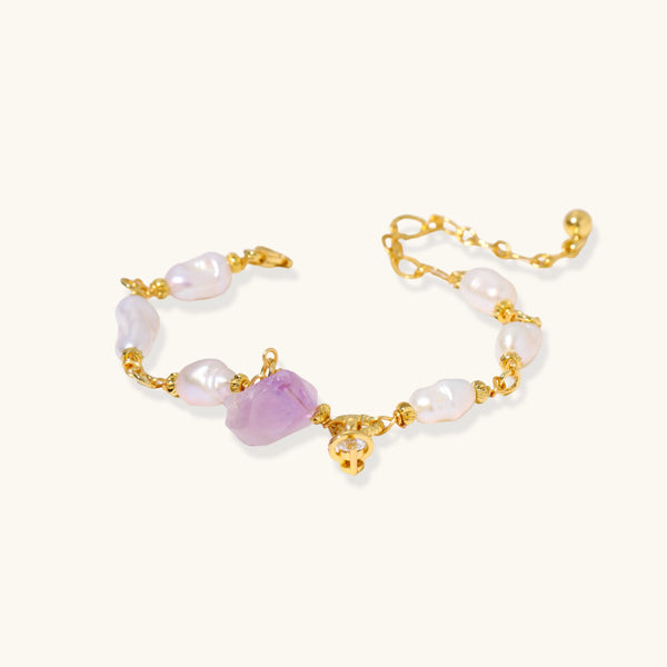 Pulsera bañada en oro con perlas barrocas lustrosas y amatista en bruto color lavanda como pieza central, sobre fondo blanco.