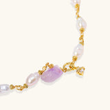 Pulsera bañada en oro con perlas barrocas lustrosas y amatista en bruto color lavanda como pieza central, sobre fondo blanco.