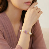 Pulsera bañada en oro con perlas barrocas lustrosas y amatista en bruto color lavanda como pieza central, sobre fondo blanco.