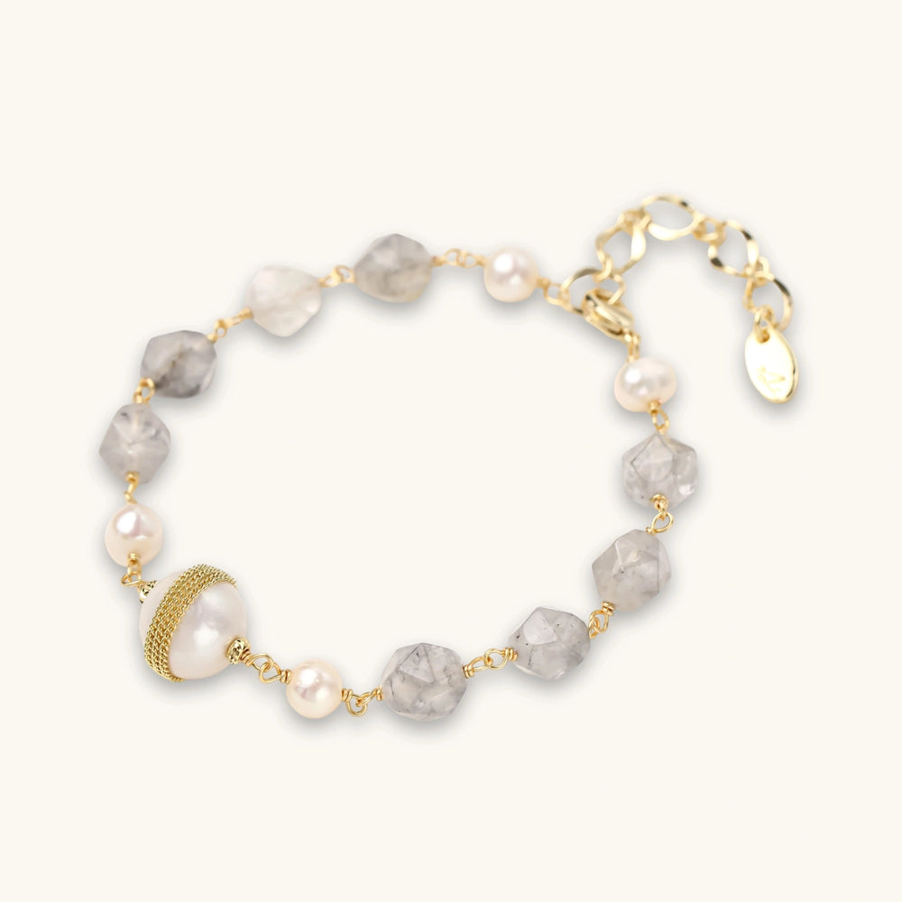 Pulsera con cuentas de cuarzo nublado, perlas de agua dulce y perla barroca central envuelta en oro, sobre fondo blanco.