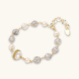 Pulsera con cuentas de cuarzo nublado, perlas de agua dulce y perla barroca central envuelta en oro, sobre fondo blanco.