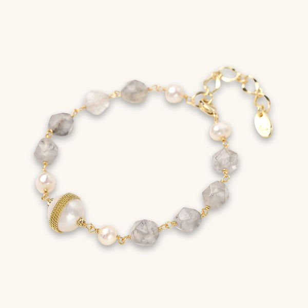 Pulsera con cuentas de cuarzo nublado, perlas de agua dulce y perla barroca central envuelta en oro, sobre fondo blanco.