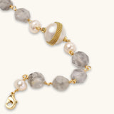 Pulsera con cuentas de cuarzo nublado, perlas de agua dulce y perla barroca central envuelta en oro, sobre fondo blanco.