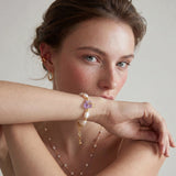 Pulsera bañada en oro con perlas barrocas lustrosas y amatista en bruto color lavanda como pieza central, sobre fondo blanco.